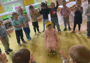 Dziewczynka w koronie siedzi pośrodku dzieci