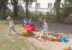Grupa dzieci bawi się plastikowymi zabawkami w piaskownicy.