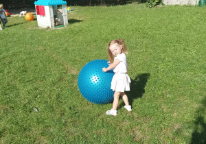 Dziewczynka bawi się w ogrodzie dużą, niebieską piłką.