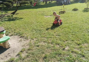 Chłopiec jeździ po trawie na plastikowym samochodziku.