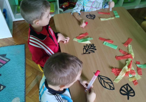 Dzieci tworzą jesiennego liścia przyklejając kolorową bibułę