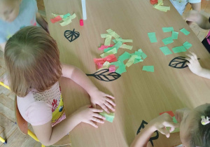 Dzieci przyklejają kolorową bibułę tworząc jesiennego liścia