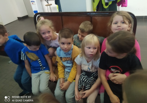 Dzieci siedzą na brązowej ławce w muzeum mpk