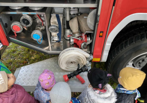Grupa dzieci ogląda sprzęt znajdujący się u wozie strażackim.