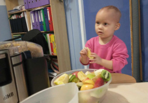 Dziewczynka stoi przy misce z owocami.