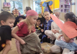 Dzieci w magicznych przebraniach siedzą w kole na dywanie i wróżą sobie.