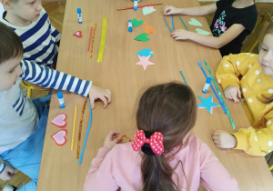 Dzieci wykonują pracę plastyczną przy użyciu kolorowej wstążki i słomki