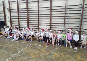 Dzieci siedzą na sali gimnastycznej w kostiumach gimnastycznych i świątecznych ozdobach