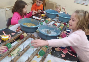 Dzieci stoją wokół stołu z brokatem, klejem i bombkami, które samodzielnie dekorują