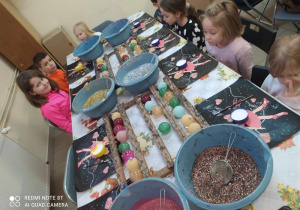 Dzieci stoją wokół stołu z brokatem, klejem i bombkami, które samodzielnie dekorują
