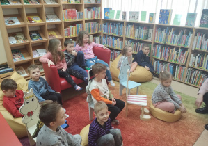 Dzieci siedzą na dywanie, poduszkach, kanapie i oglądają różne książki