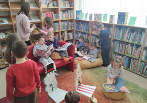 Dzieci siedzą na dywanie, poduszkach, kanapie i oglądają różne książki