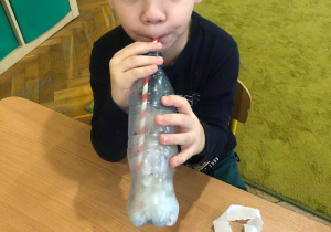 Chłopiec wydmuchuje powietrze do butelki