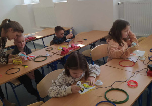 Dzieci biorą udział w zajęciach z robotyki i pracują długopisami 3d