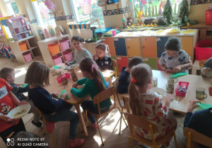 Dzieci siedzą przy stolikach i jedzą wielkanocne potrawy