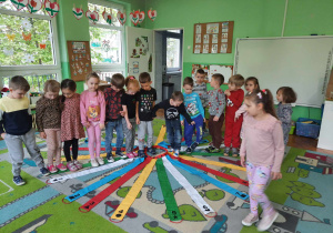 Dzieci stoją na dywanie i wykonują polecenia nauczyciela