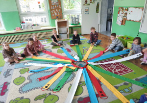 Dzieci siedzą na dywanie i wykonują polecenia nauczyciela