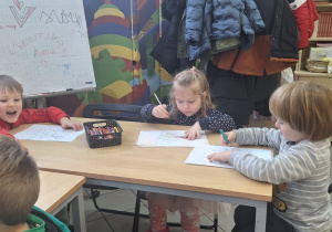 Dzieci są z wizytą w bibliotece. Dookoła widać regały z książkami i kolorowe ściany