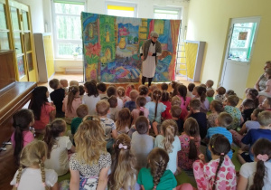 Na zdjęciu widzimy grupę dzieci siedzących na dywanie i oglądających przedstawienie teatralne