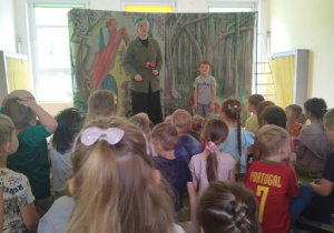 Na zdjęciu widzimy grupę dzieci siedzących na dywanie i oglądających przedstawienie teatralne