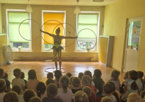 Kobieta w stroju scenicznym wykonuje pokaz z obręczami hula-hop, trzymając kilka kół jednocześnie.