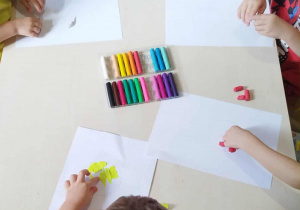 Dzieci siedzą przy stoliku i wykonują prace plastyczną z plasteliny