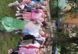 Dzieci stoją z workami śmieci. W tle widać drzewa i zieleń