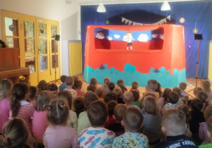 Dzieci siedzą na dywanie i oglądają przedstawienie