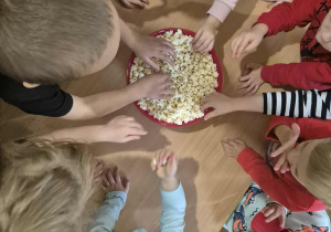 Dzieci jedzą popcorn.