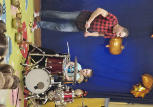 Mężczyzna gra na instrumentach - perkusji i bębnach, dzieci obserwują go.