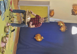 Mężczyzna gra na instrumentach - perkusji i bębnach, dzieci obserwują go.