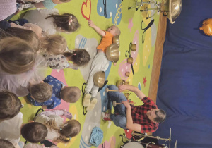 Mężczyzna gra na instrumentach - perkusji i bębnach, dzieci obserwują go.