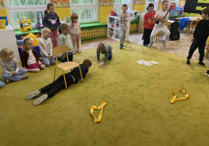 Chłopiec przechodzi pod krzesłem, dzieci patrzą na niego