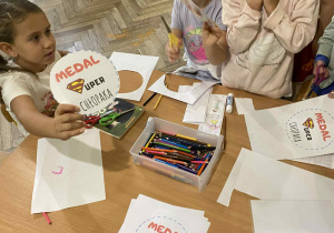 Dziewczynki przy stoliku przygotowują medale dla chłopaków