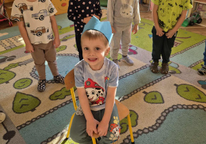 Franek siedzi na krześle w koronie. Dookoła są dzieci, które otaczają go w kole i śpiewają sto lat.