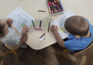 dzieci siedzą przy stoliku i kolorują prace