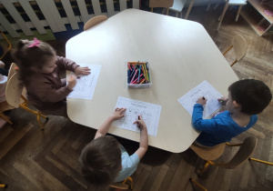dzieci siedzą przy stoliku i kolorują prace