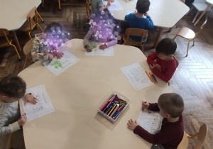 dzieci siedzą przy stoliku i kolorują prace