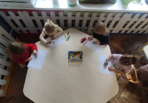 dzieci siedzą przy stoliku i kolorują prace