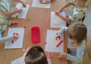 Dzieci wykonują prace plastyczną wyklejają serca bibułą w kolorach narodowych