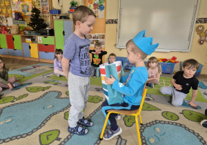 Chłopiec w koronie siedzi na krześle a drugi chłopiec składa mu życzenia i bierze prezent.