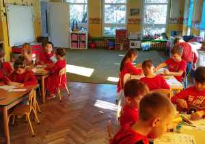 Dzieci siedzą przy stolikach wykonują pracę plastyczną
