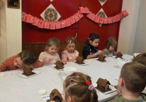 Dzieci biorą udział w warsztatach świątecznych. Robią stroiki i dekorują domki z piernika