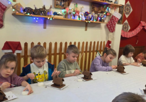 Dzieci biorą udział w warsztatach świątecznych. Robią stroiki i dekorują domki z piernika