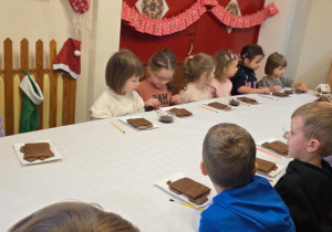 Dzieci biorą udział w warsztatach świątecznych. Robią stroiki i dekorują domki z piernika
