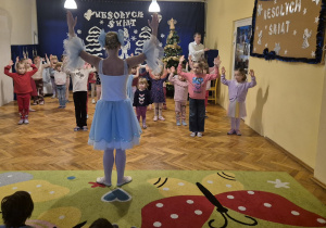 Tancerka uczy dzieci tańca robotów. Kobieta unosi ręce do góry.