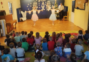 Dzieci siedzą na dywanie i oglądają pokaz tańców z bajek