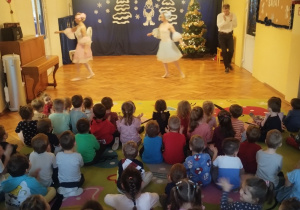 Dzieci siedzą na dywanie i oglądają pokaz tańców z bajek