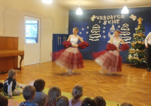 Dzieci siedzą na dywanie i oglądają pokaz tańców z bajek