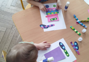 dwójka dzieci wykonuje pracę plastyczną, tworząc roboty z kolorowych elementów